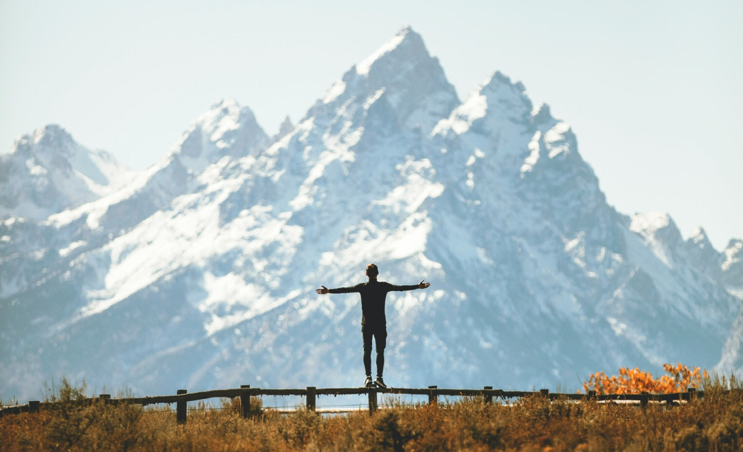 Distant silhouette picture of a man alone in view of mountains with his arms stretched out.